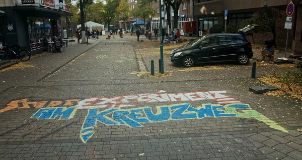 Bunte Straßenbemalung mit der Aufschrift „Stadtexperimente am Kreuzweg“ in einer herbstlichen Innenstadtstraße.